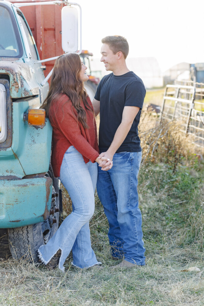 engaged couple pose with a turquoise truck on a farm in Montana