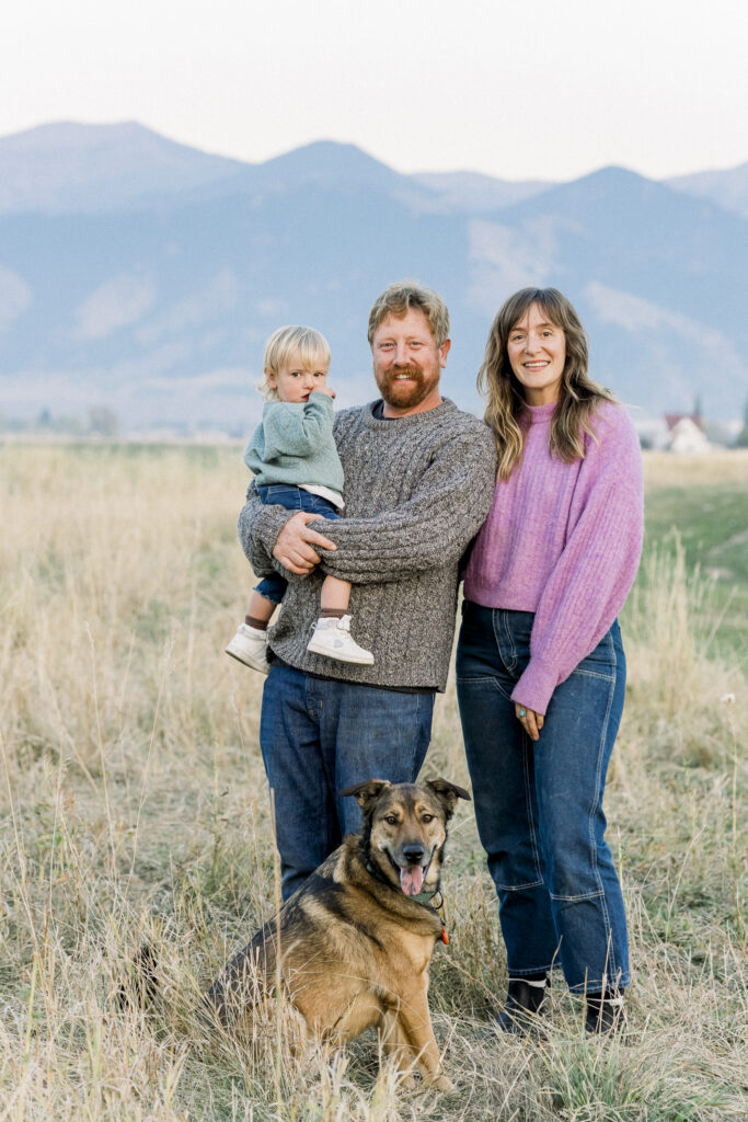 mom, dad, and toddler with family dog in front of Bridger mountains