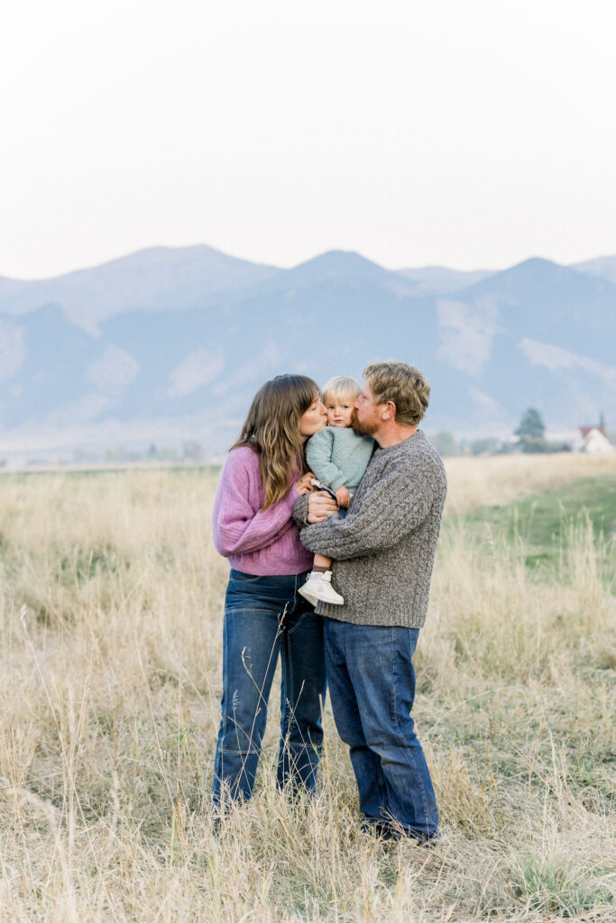 mom and dad give toddler girl a kiss in front of Bridger mountains